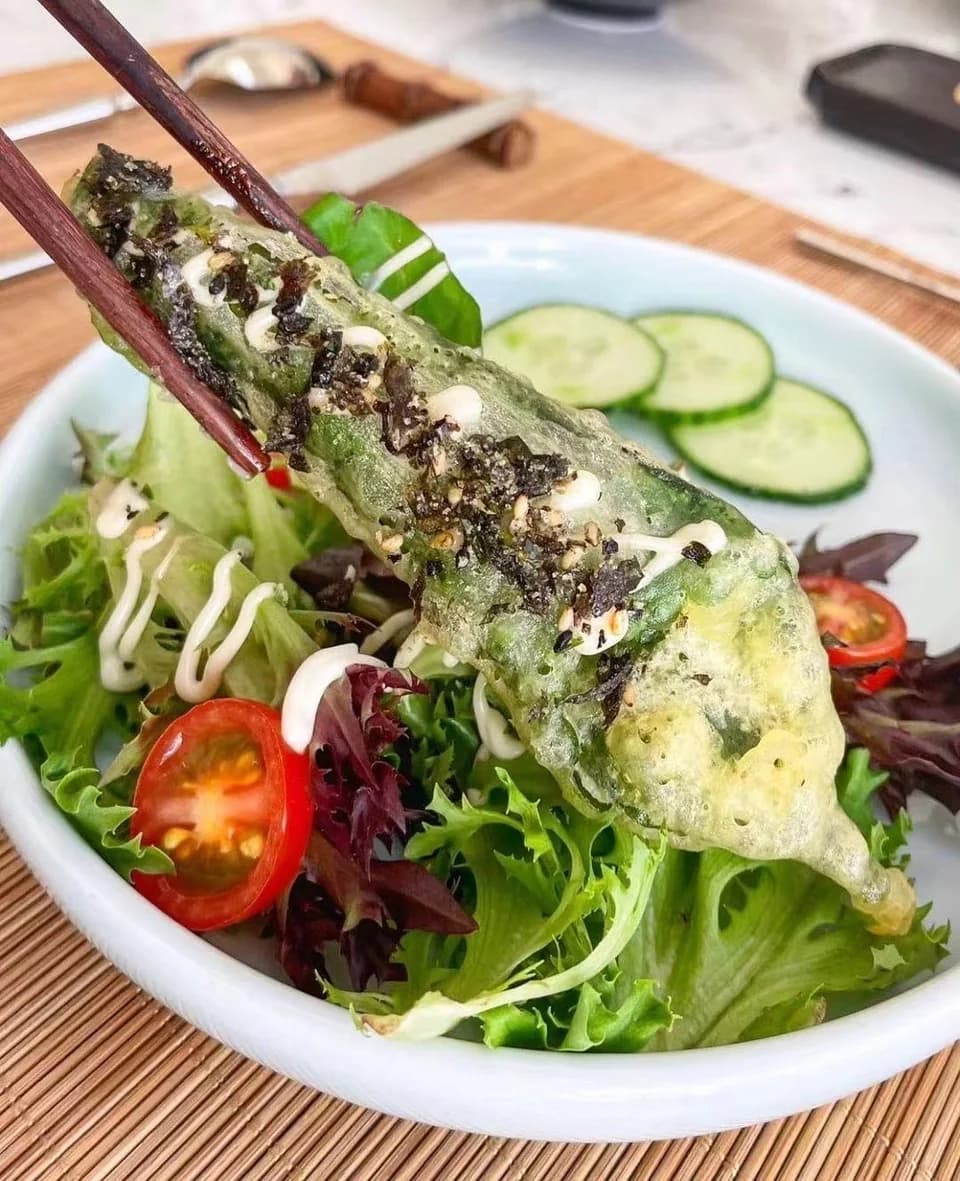 Crisp perilla tempura lifted with chopsticks above fresh greens