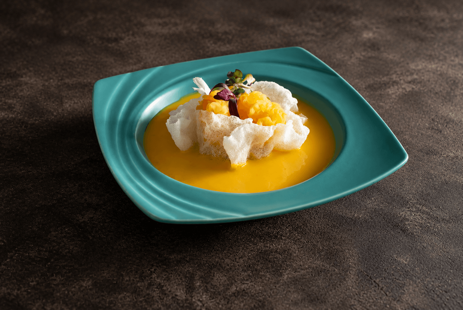 Golden pumpkin soup with delicate crisp garnish in a turquoise bowl